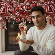 Candy Cane Crossing ornament held in hand, red and white striped design with fireplace backdrop