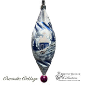 Cascades Cottage ornament with blue winter scene, snow-covered cottage, and burgundy ball finial.