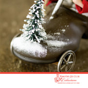 Driving Shoe Crazy Santa ornament with snow-dusted finish and evergreen sprig on vintage toy wheel base
