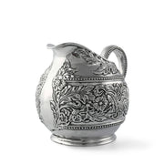 Concho Pattern Pitcher, silver metal with ornate embossed florals and beaded borders, angled view showing handle and spout.
