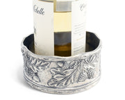 Acorn Oak & Leaf Pewter Wine Coaster holding white wine bottle with decorative grape and leaf relief design